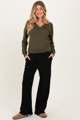 woman wearing an olive green v-neck maternity top and black wide-leg maternity pants with pockets
