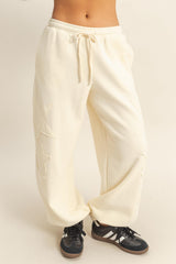 woman wearing cream-colored sweatpants with star embroidery and a drawstring waist, paired with black sneakers