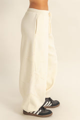woman wearing cream colored wide leg sweatpants with star embroidery and a drawstring waist