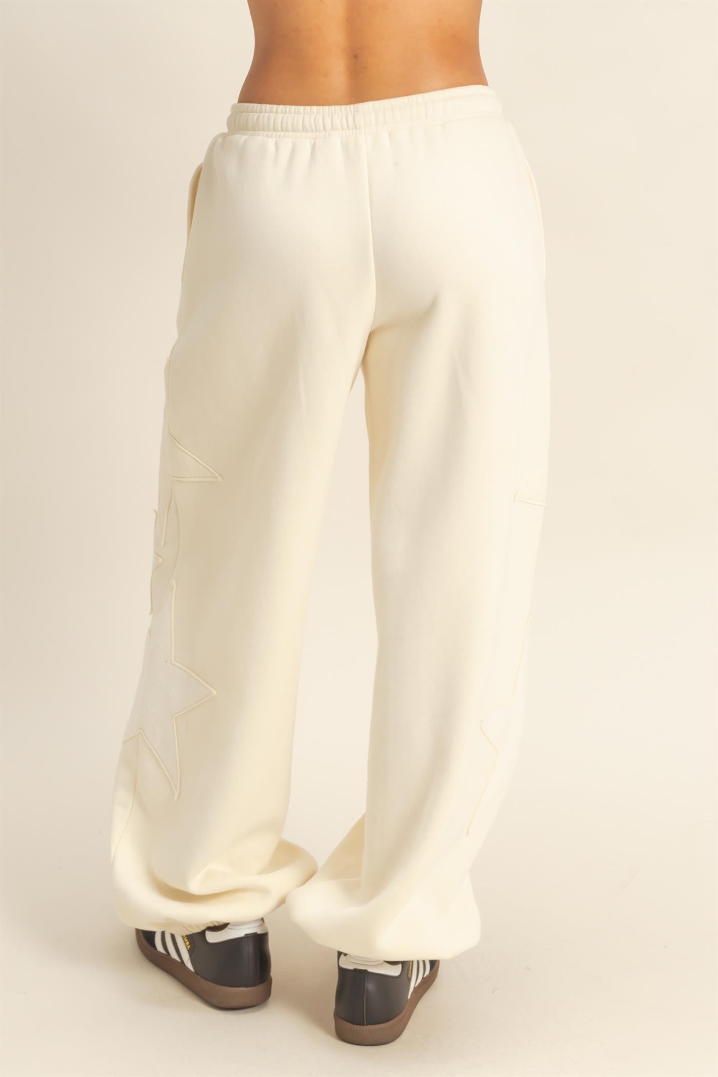 woman wearing cream-colored wide-leg sweatpants with star embroidery on the sides, viewed from the back