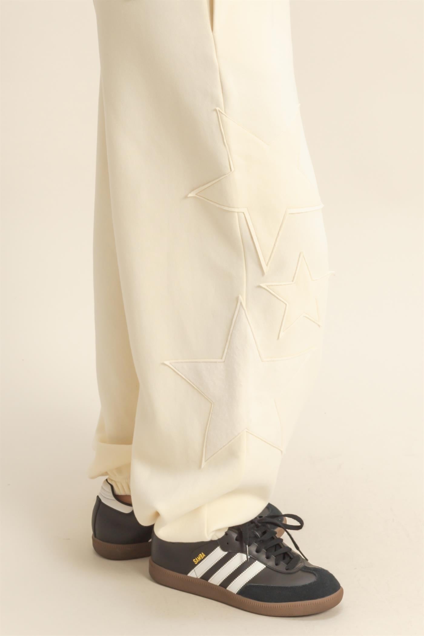 woman wearing cream-colored sweatpants with star embroidery and black sneakers with white stripes