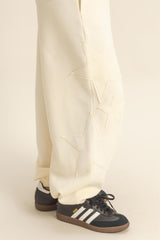 woman wearing cream-colored sweatpants with star embroidery and black sneakers with white stripes