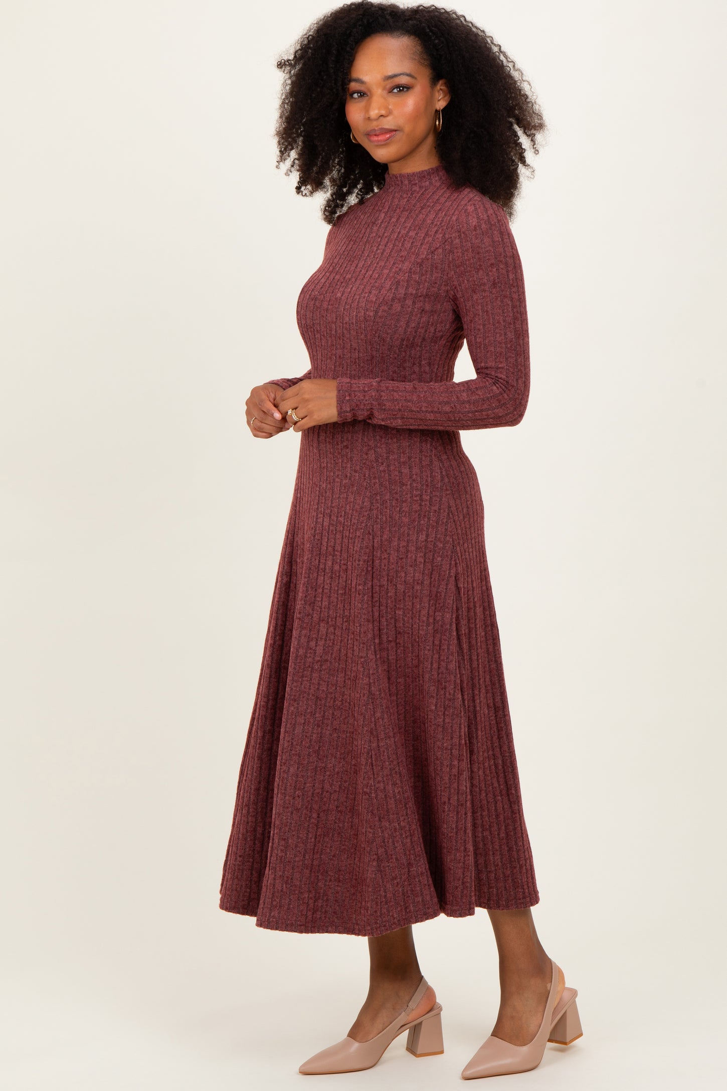 woman wearing a burgundy ribbed long sleeve midi dress with a fitted bodice and flared skirt, styled with beige heels