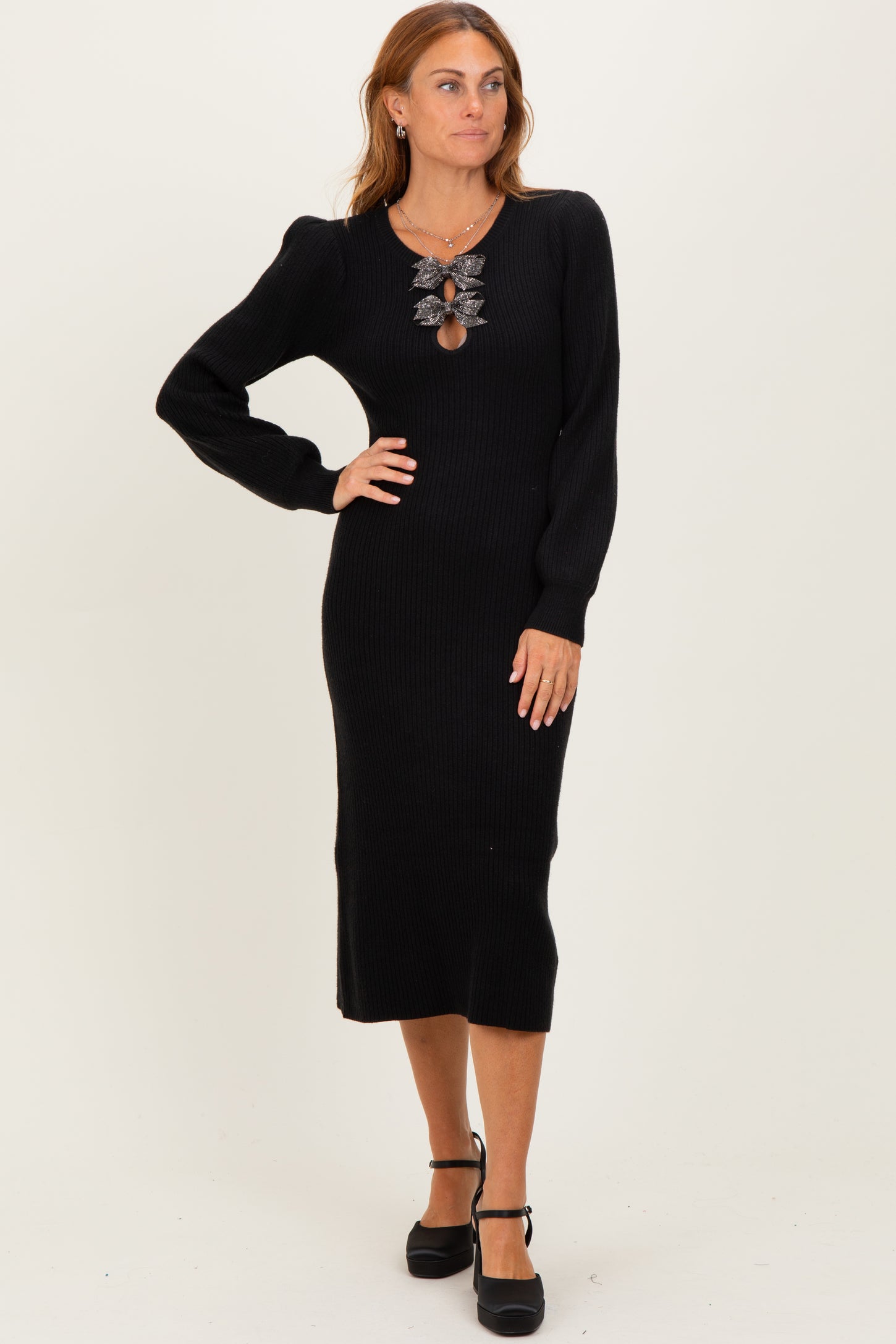 woman wearing a black ribbed long sleeve midi dress with a decorative necklace and posing with one hand on her hip