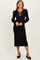 woman wearing a black ribbed long sleeve midi dress with a decorative bow detail and heels