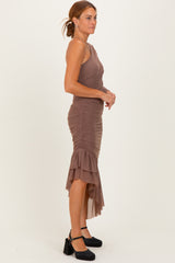 woman wearing a taupe one-shoulder ruched dress with a frilled hem and heeled black shoes