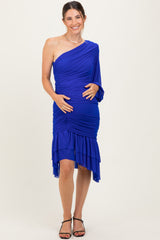 woman wearing a royal blue one-shoulder maternity dress with ruched detailing and a high-low hem, gently cradling her baby bump