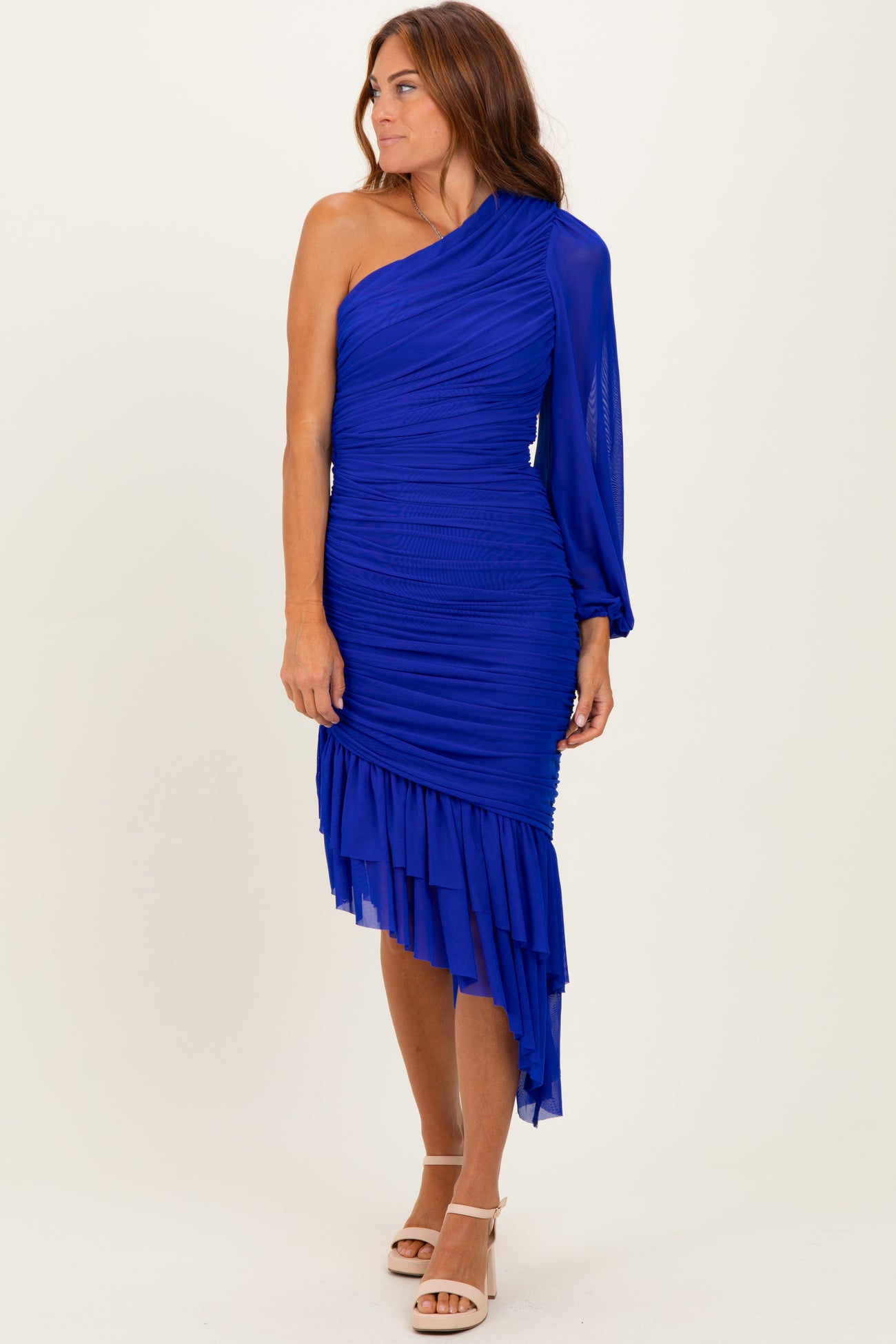 woman wearing a royal blue one-shoulder ruched dress with a draped hem and long sleeve detail