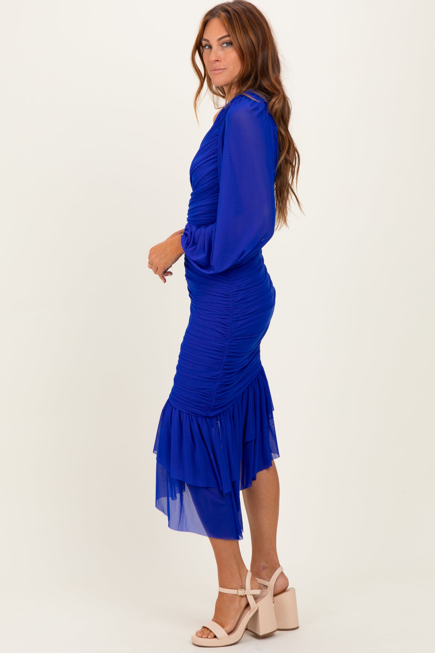 woman wearing a fitted royal blue dress with ruched detailing and a layered chiffon hem