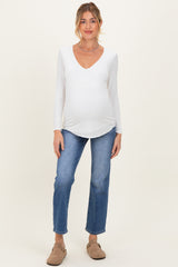 woman wearing a white long sleeve maternity top and blue jeans, showing her baby bump