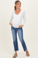 woman wearing a white long sleeve maternity top and blue jeans, showing her baby bump