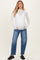 woman wearing a white long sleeve maternity top with textured pattern and blue relaxed-fit maternity jeans, showing her baby bump