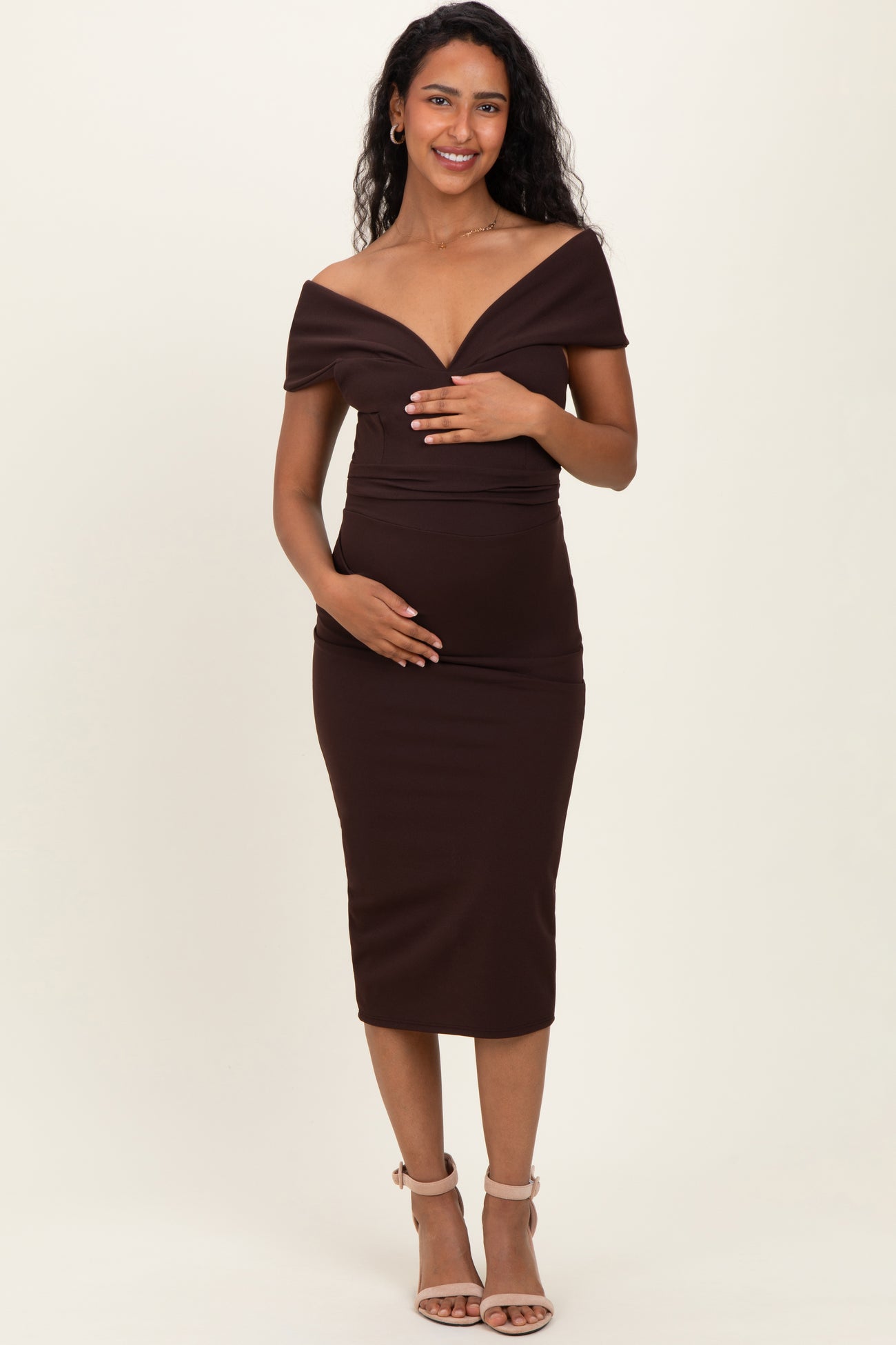 woman wearing a brown off-the-shoulder maternity dress and holding her baby bump