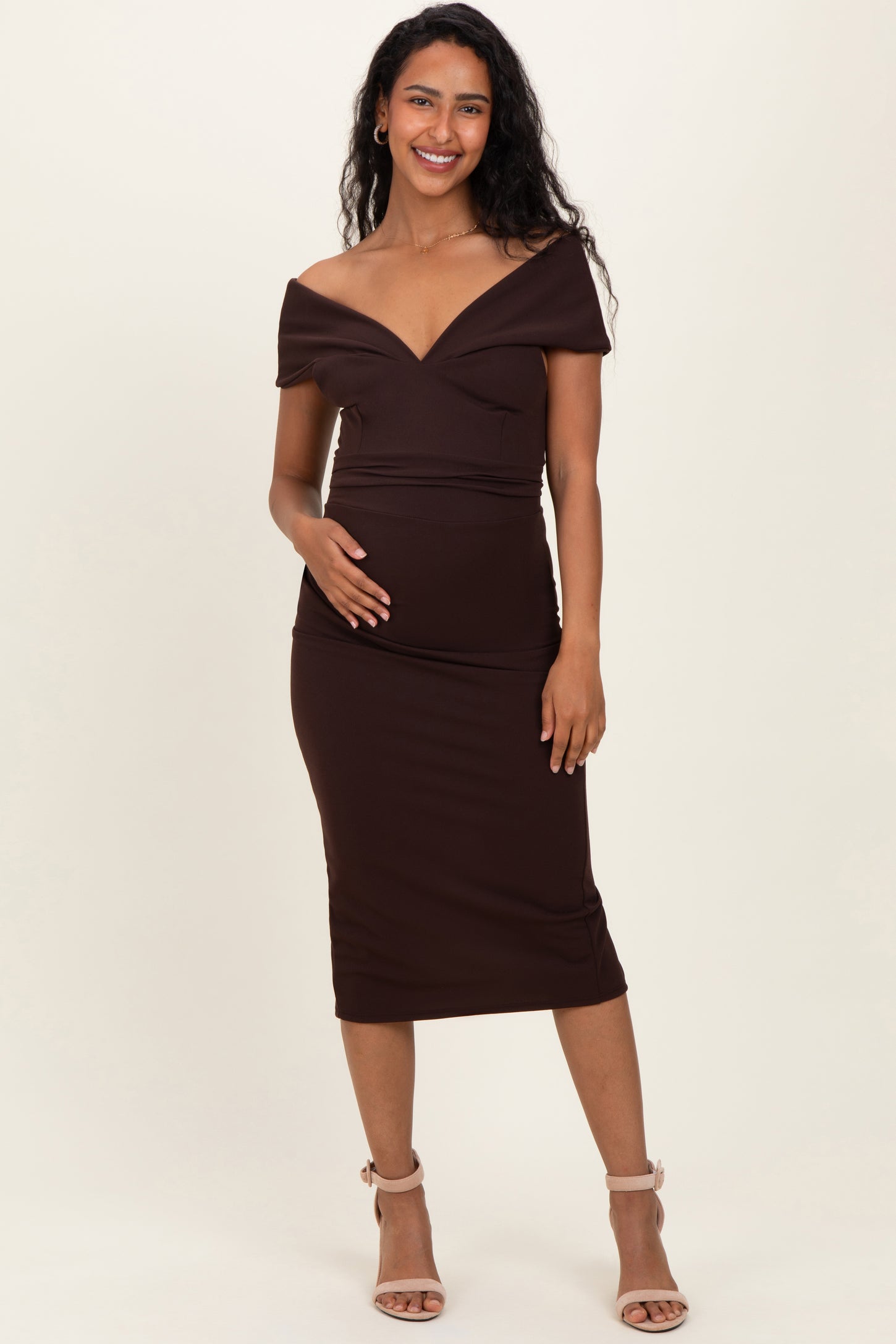 woman wearing a brown off-the-shoulder maternity dress with a fitted silhouette and holding her baby bump