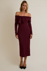 woman wearing a burgundy off-the-shoulder ribbed midi dress with a bow detail and long sleeves