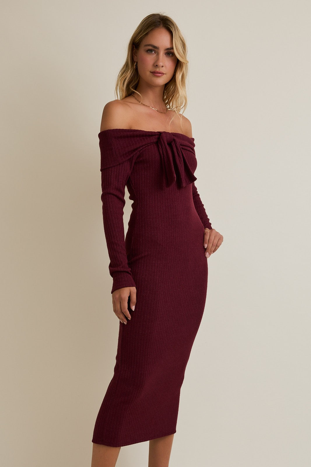 woman wearing a burgundy off-shoulder fitted dress with long sleeves and a bow detail on the chest