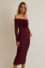 woman wearing a burgundy off-shoulder fitted dress with long sleeves and a bow detail on the chest