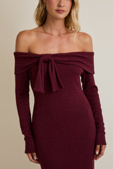 woman wearing a burgundy off-the-shoulder ribbed dress with long sleeves and a tie detail at the neckline