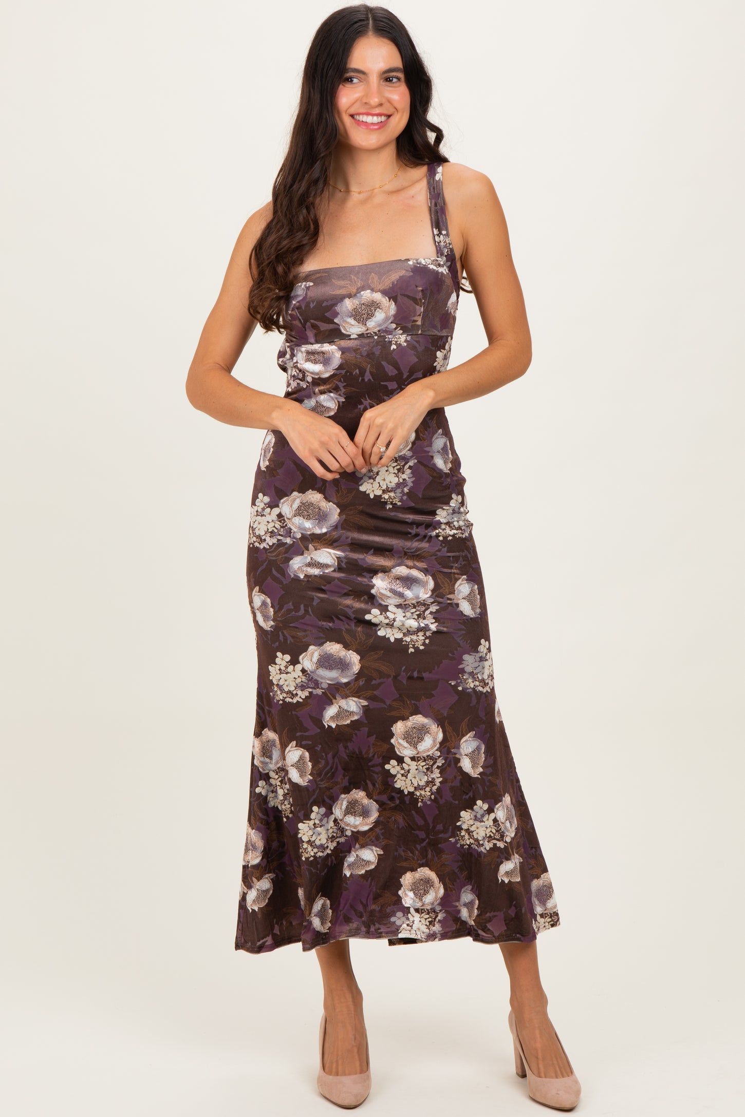 woman wearing a brown floral midi dress with a fitted bodice and flared hem, smiling and posing with one hand on her hip