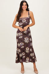 woman wearing a brown floral midi dress with a fitted bodice and flared hem, smiling and posing with one hand on her hip