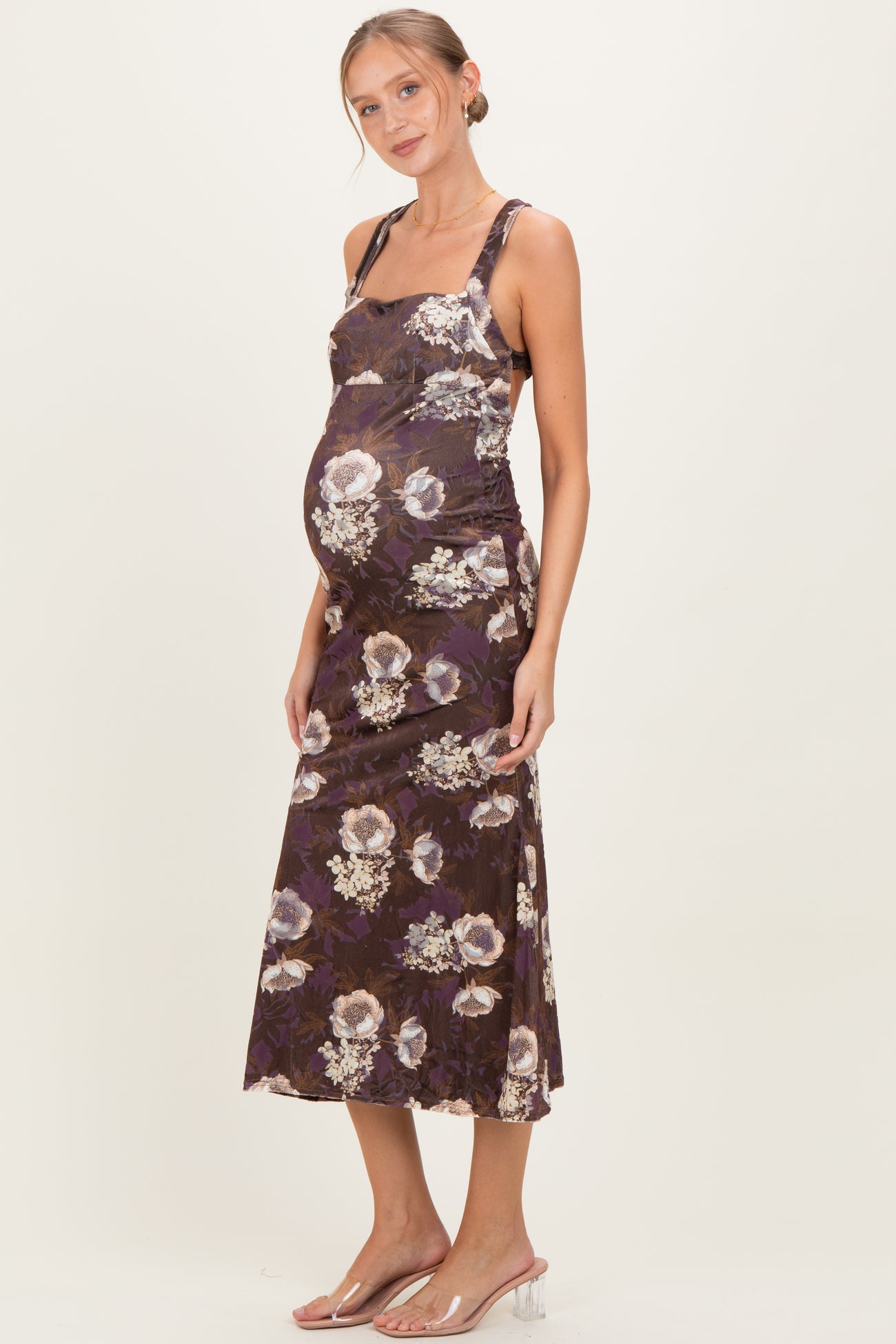 woman wearing a purple floral maternity dress and highlighting her baby bump