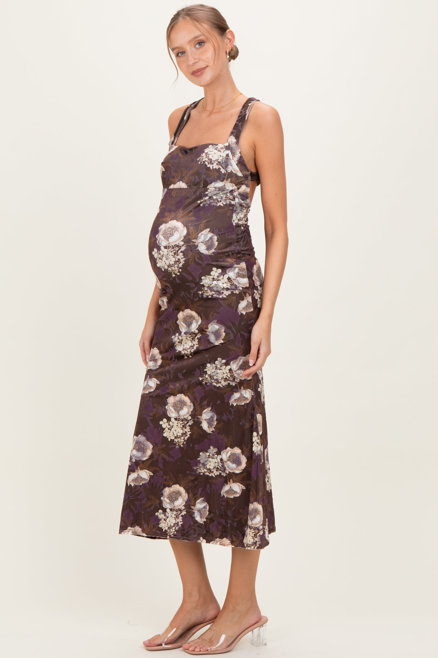 woman wearing a purple floral maternity dress and highlighting her baby bump