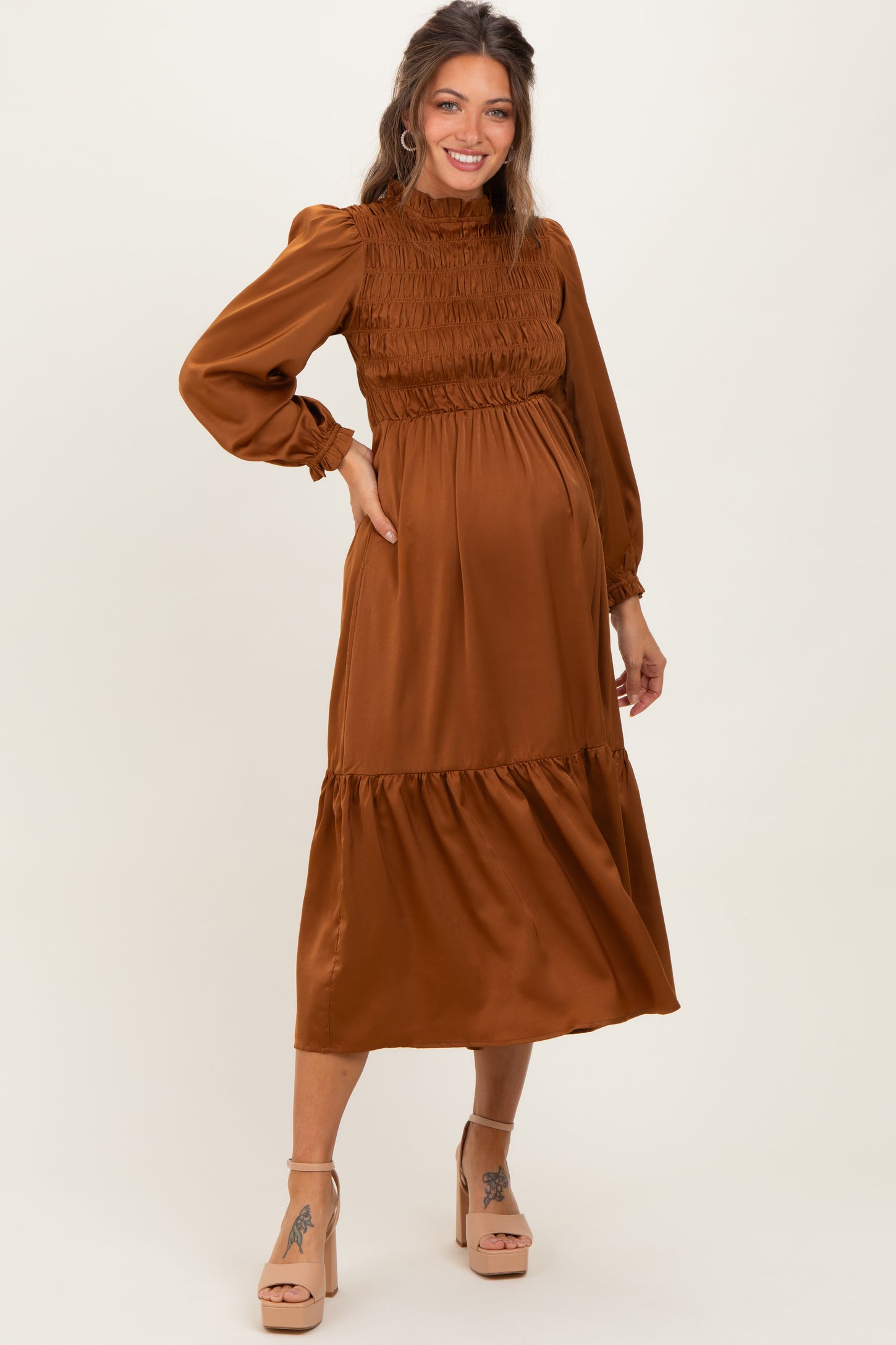 woman wearing a rust-colored maternity dress with smocking details and long sleeves, showcasing her baby bump
