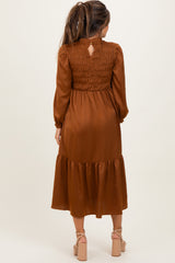 woman wearing a rust brown maternity dress with a smocked back and tiered skirt, showing a baby bump