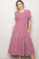 woman wearing a mauve puff sleeve maxi dress with a smocked bodice and tiered skirt, posing with hands in pockets