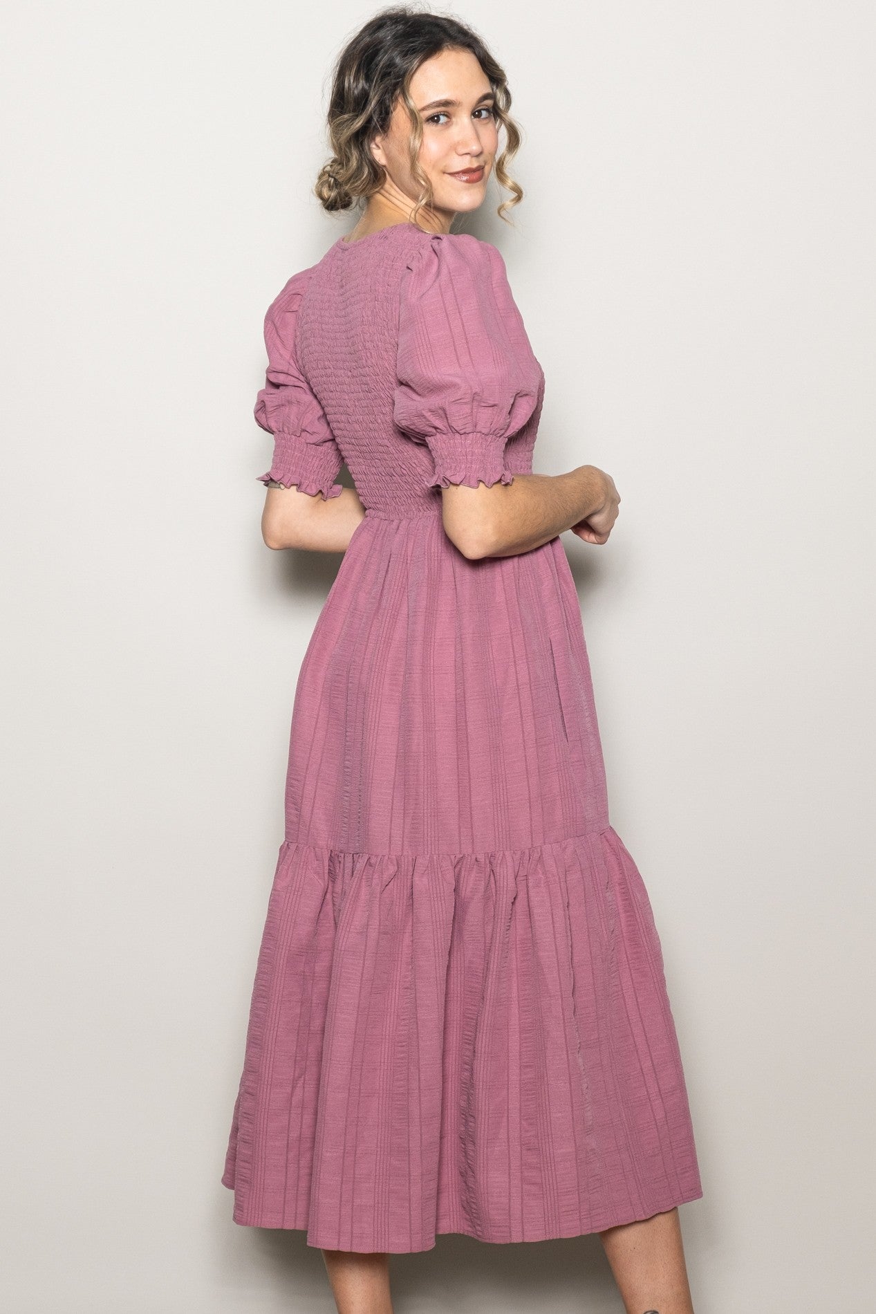 woman wearing a dusty pink midi dress with puff sleeves and a tiered skirt, shown from the back