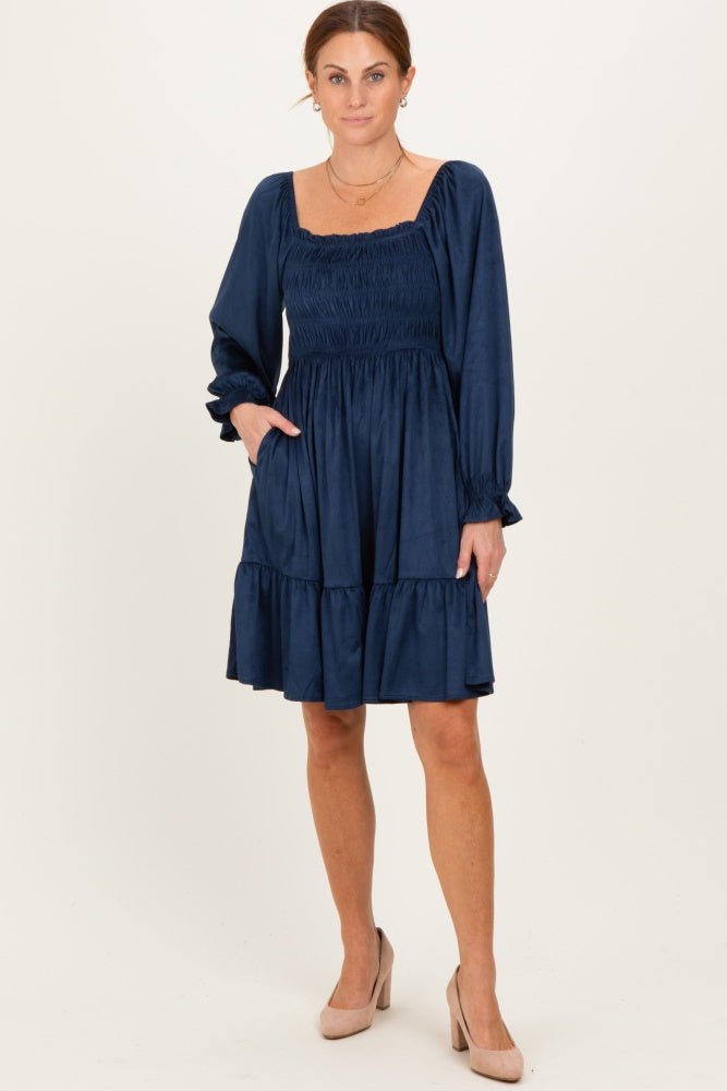 woman wearing a navy blue long sleeve smocked dress with a tiered skirt and pockets, standing in nude high heels
