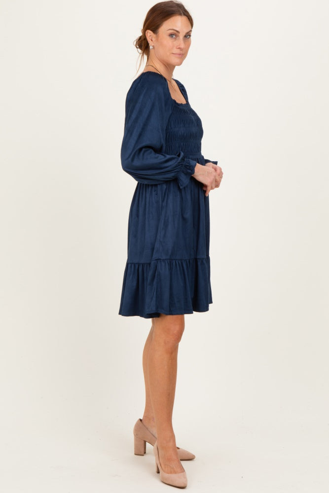 woman wearing a navy blue smocked dress with puff sleeves and a tiered ruffle hem, standing in profile with heels