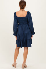 woman wearing a navy blue smocked back dress with long sleeves and a tiered skirt, standing with her back to the camera