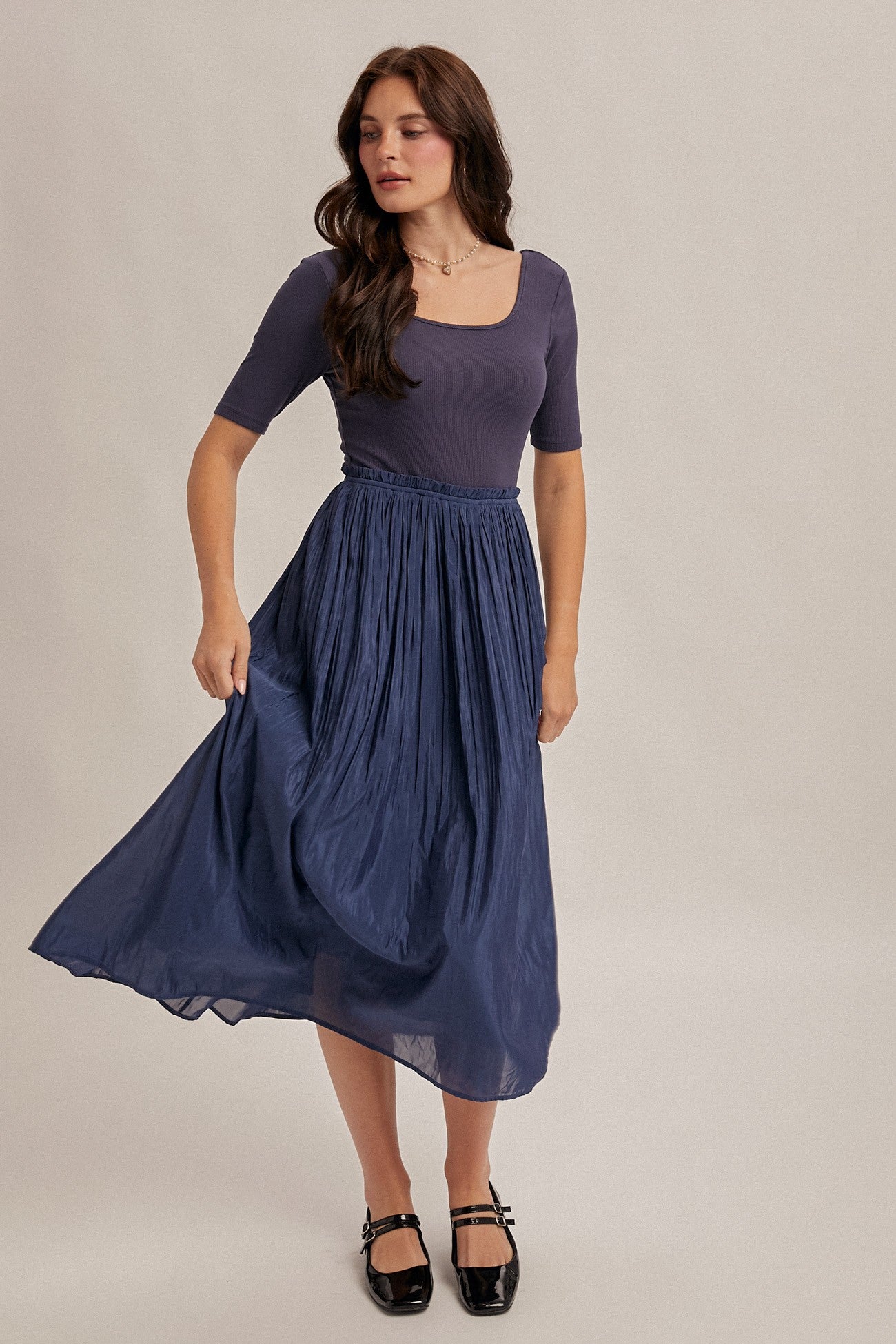 woman wearing a navy blue ribbed top and a flowing pleated maxi skirt