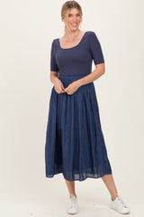 woman wearing a navy blue fitted top with a square neckline and a pleated midi skirt, paired with white sneakers