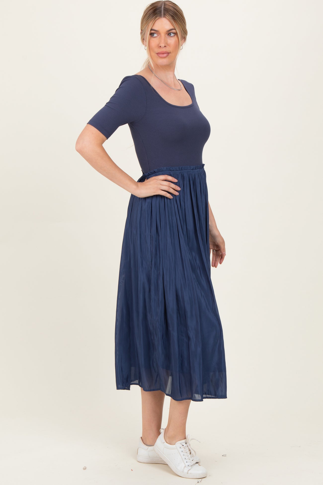 woman wearing a navy blue short sleeve dress with a fitted top and flowy midi skirt, paired with white sneakers