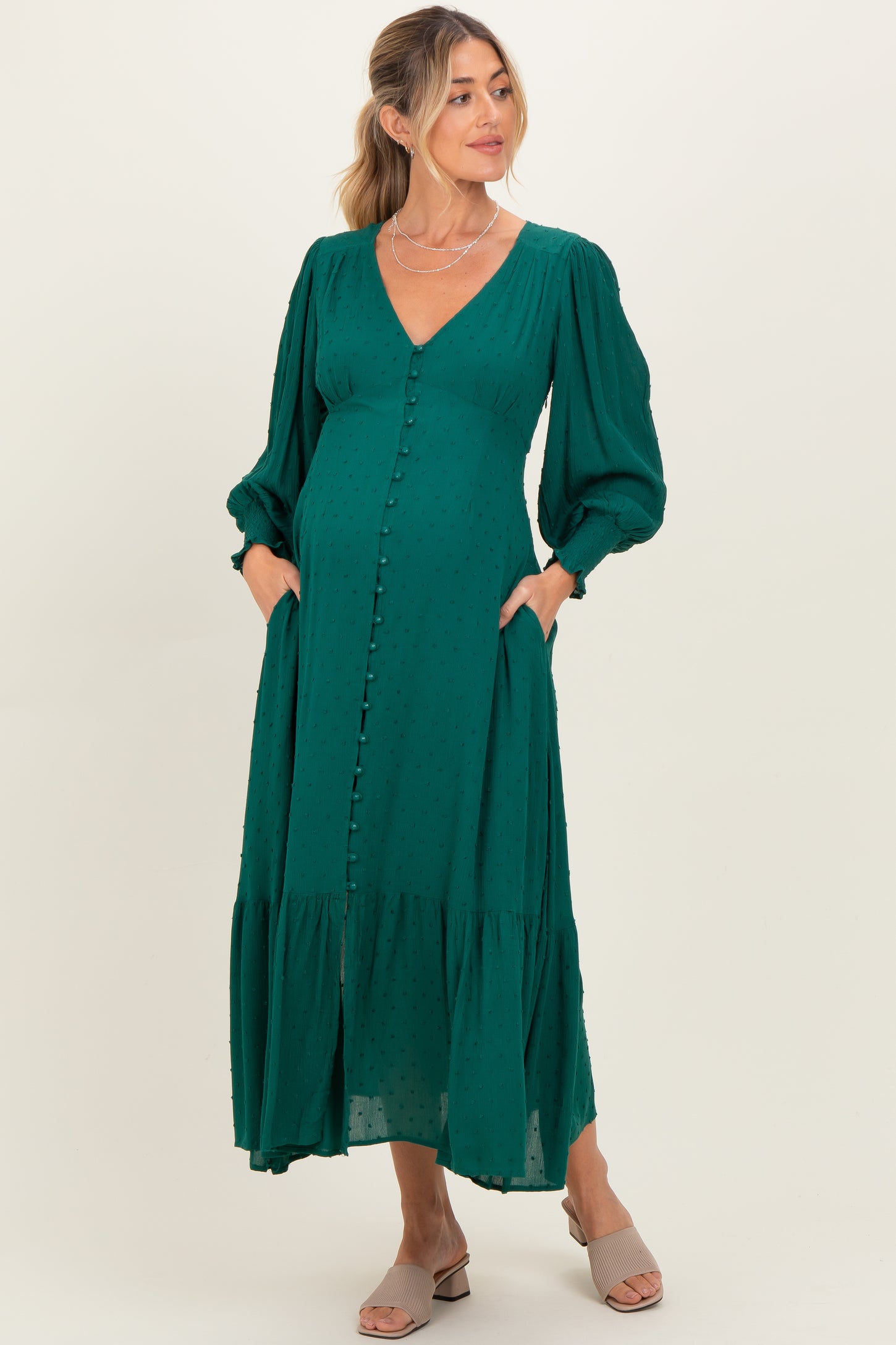 woman wearing a green maternity dress with a v-neck, puff sleeves, and pockets, holding her baby bump