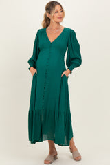 woman wearing a green maternity dress with a v-neck, puff sleeves, and pockets, holding her baby bump