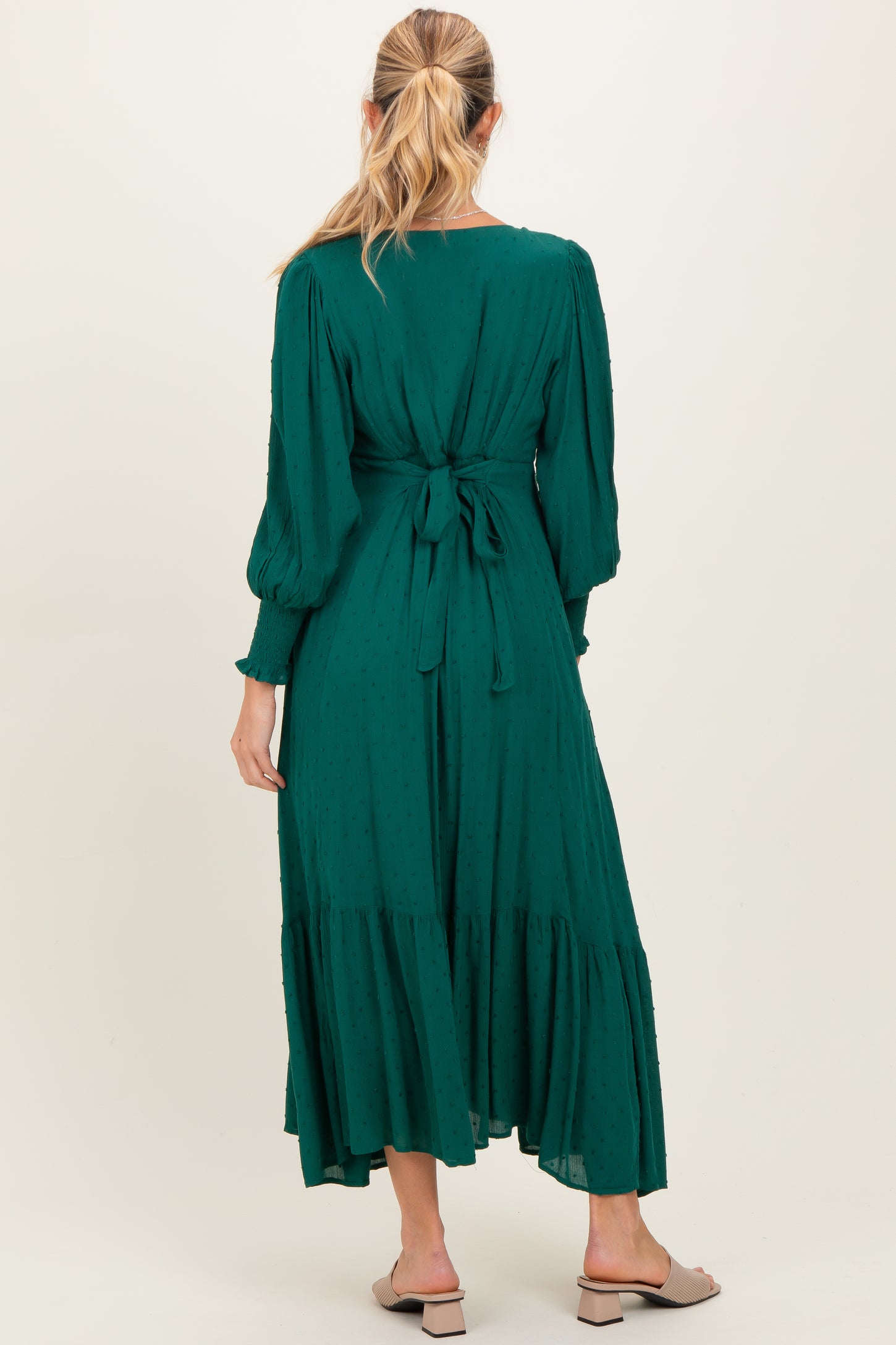 woman wearing a green long sleeve maternity dress with a tied back detail and a flowy tiered skirt