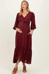 woman wearing a burgundy maternity dress with buttons, a tie waist, and long sleeves, showing a baby bump