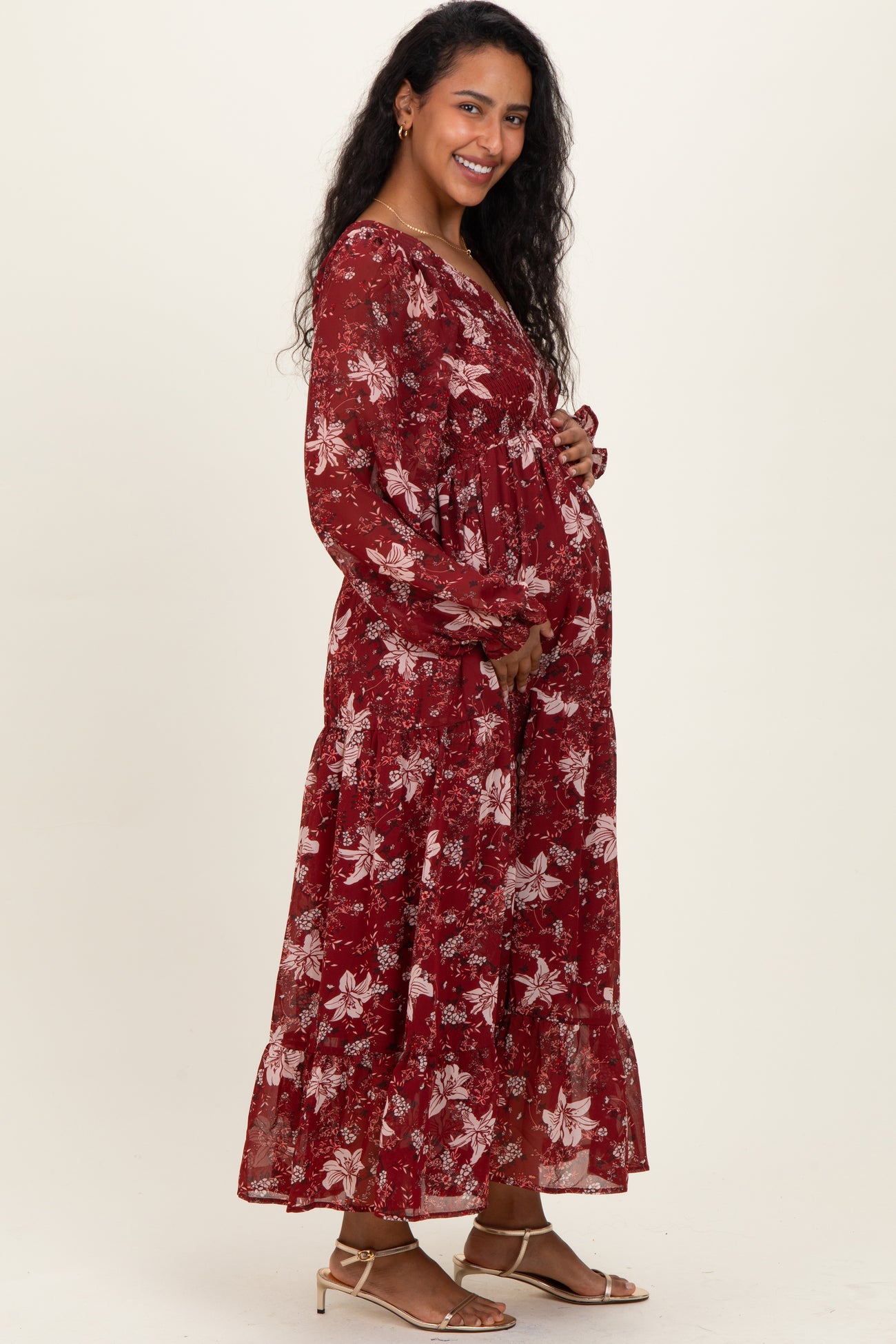 woman wearing a burgundy floral long sleeve maternity dress and holding her baby bump