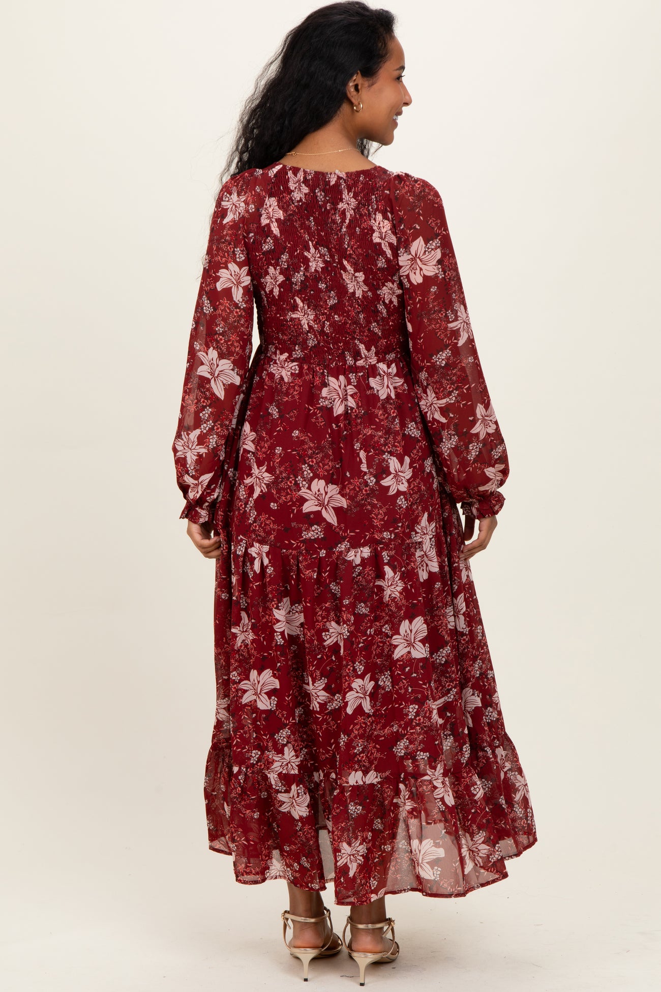 woman wearing a burgundy floral maternity maxi dress with long sleeves and a ruffled hem, showing a baby bump from behind