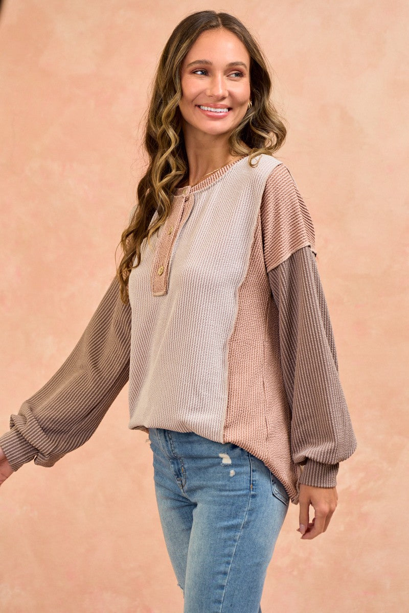 woman wearing a color-blocked long sleeve top with a henley neckline and balloon sleeves paired with skinny jeans