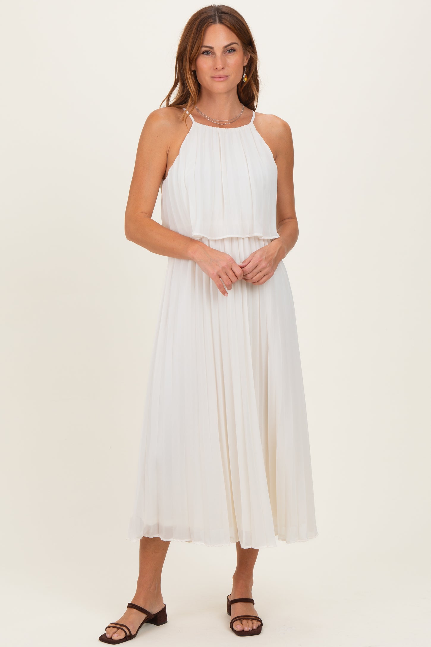 woman wearing a white pleated midi dress with a halter neckline and layered top, standing with hands clasped in front