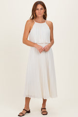 woman wearing a white pleated midi dress with a halter neckline and layered top, standing with hands clasped in front