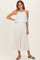woman wearing a white pleated maxi dress with a halter neckline and layered bodice, standing with one hand on her hip
