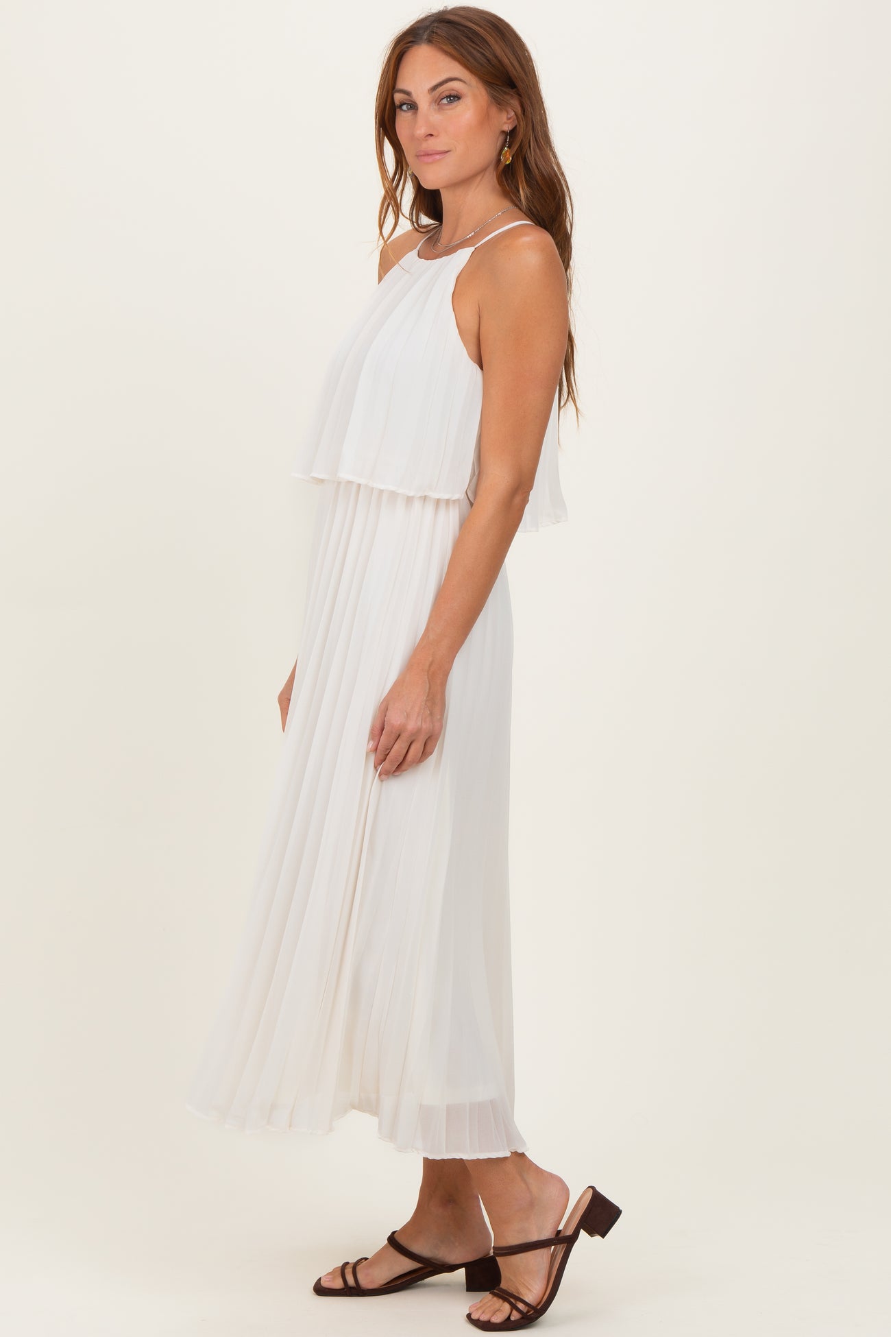 woman wearing a white flowy maxi dress with layered design and a pleated skirt, styled with strappy sandals