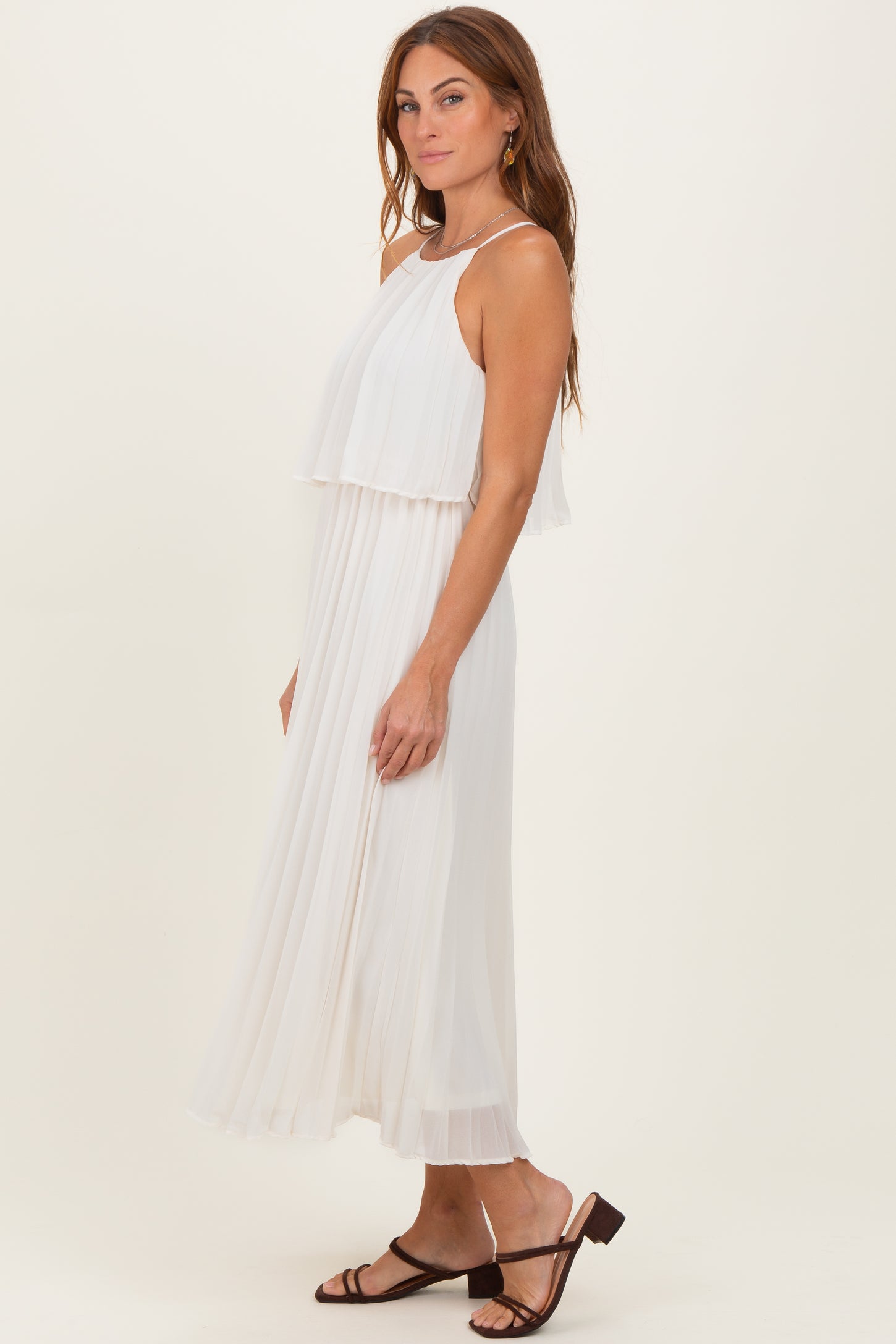 woman wearing a white flowy maxi dress with layered design and a pleated skirt, styled with strappy sandals