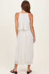 woman wearing a white pleated maxi dress with a layered back and button details, standing in a relaxed pose