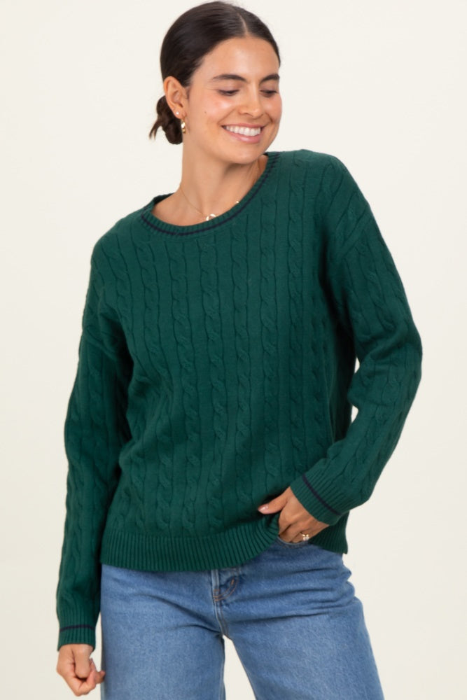 woman wearing a green cable knit sweater with a round neckline and relaxed fit, paired with denim jeans